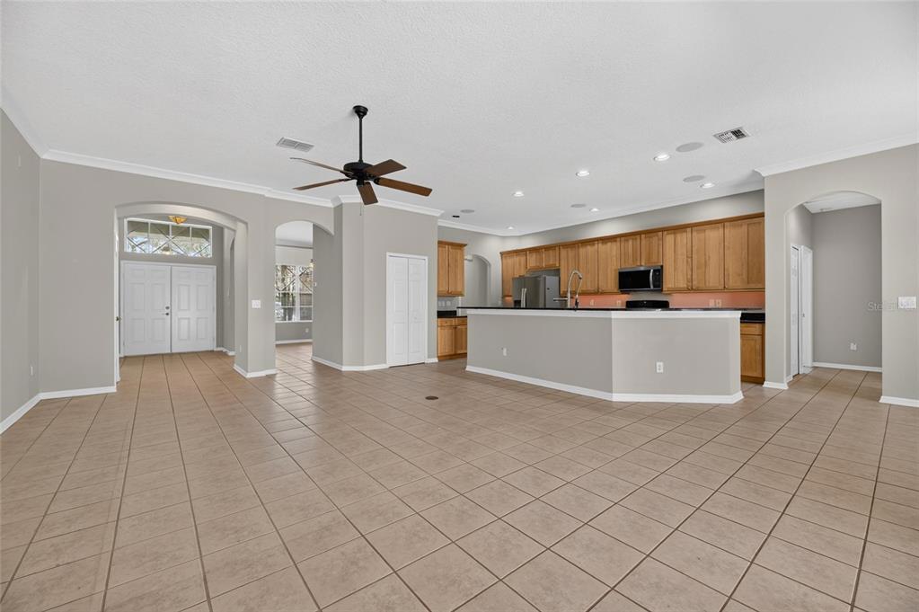 An open-concept kitchen with wood cabinets and a breakfast bar overlooks a tiled living area — 12519 RIVER BIRCH DRIVE, RIVERVIEW, FL