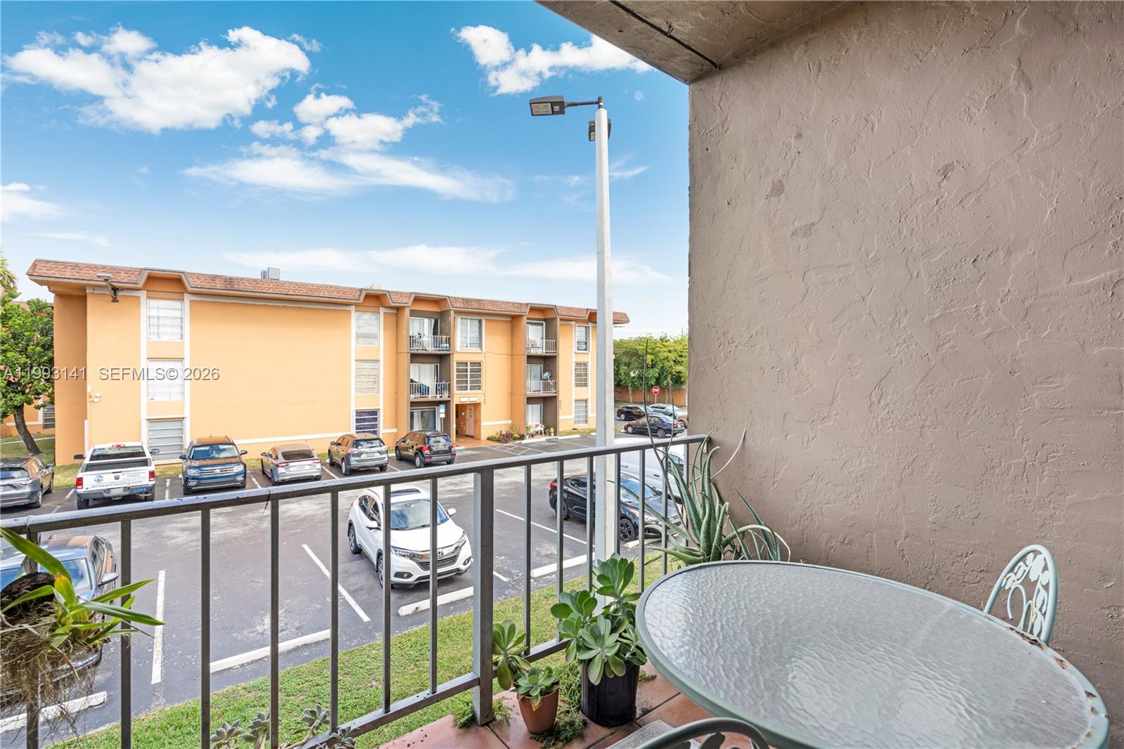 A balcony overlooks a parking lot with several cars and a neighboring apartment building — 9423 SW 76th St # W21, Miami FL 33173, MIAMI, FL