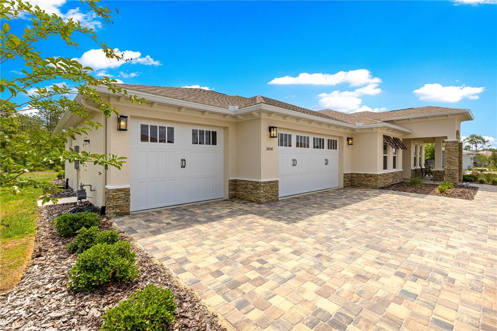 A beige house exterior features a three-car garage, stone accents, and a paved driveway — 10050 SW 106TH CIRCLE, OCALA, FL