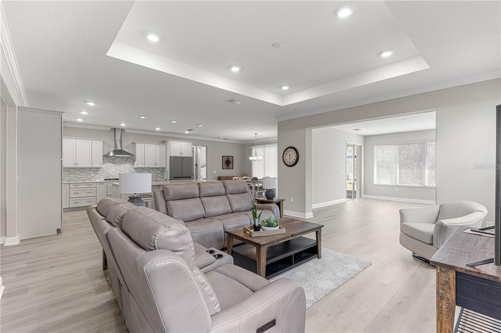 An open-concept living room features light wood flooring, a tray ceiling, and a gray sofa — 10050 SW 106TH CIRCLE, OCALA, FL