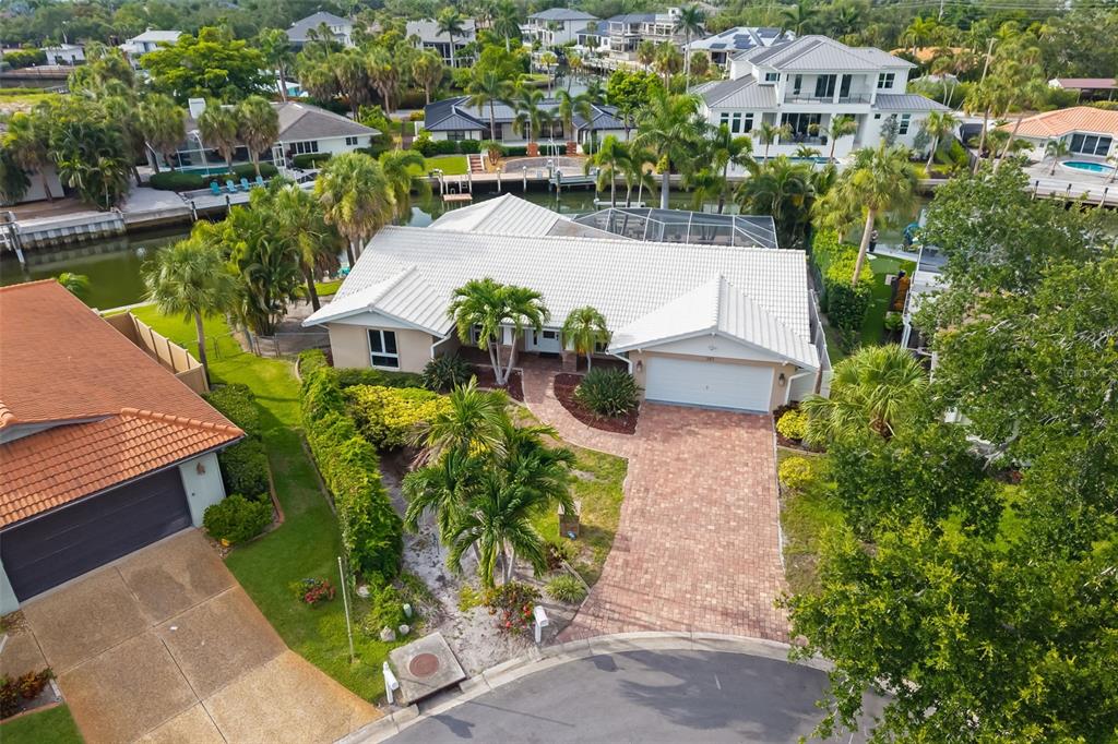 An aerial view shows a single-story house with a white roof, brick driveway, and pool — 565 COMMONWEALTH PLACE, SARASOTA, FL