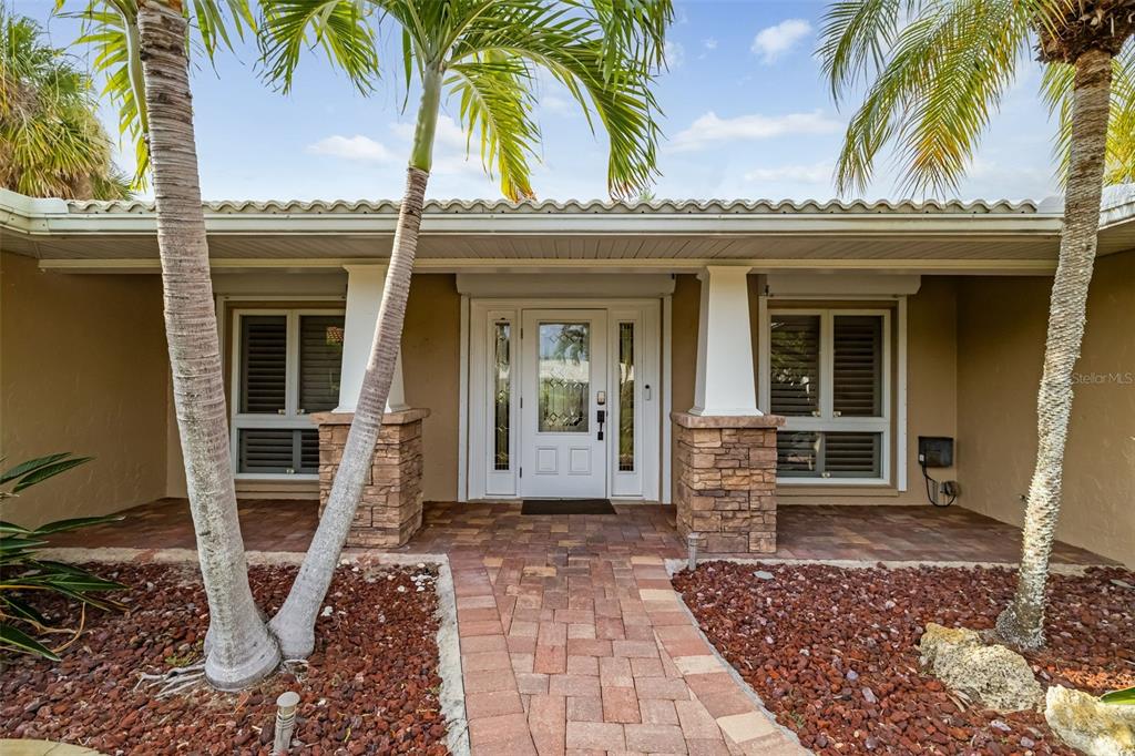 The front entrance of a house features a paved walkway, stone pillars, and palm trees — 565 COMMONWEALTH PLACE, SARASOTA, FL