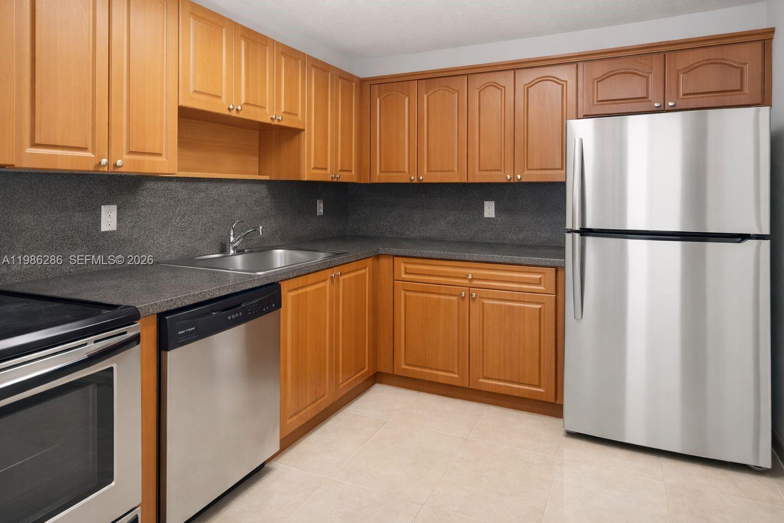 A kitchen features wood cabinets, stainless steel appliances, and dark gray countertops — 15620 SW 80th St # 304, Kendall FL 33193, KENDALL, FL