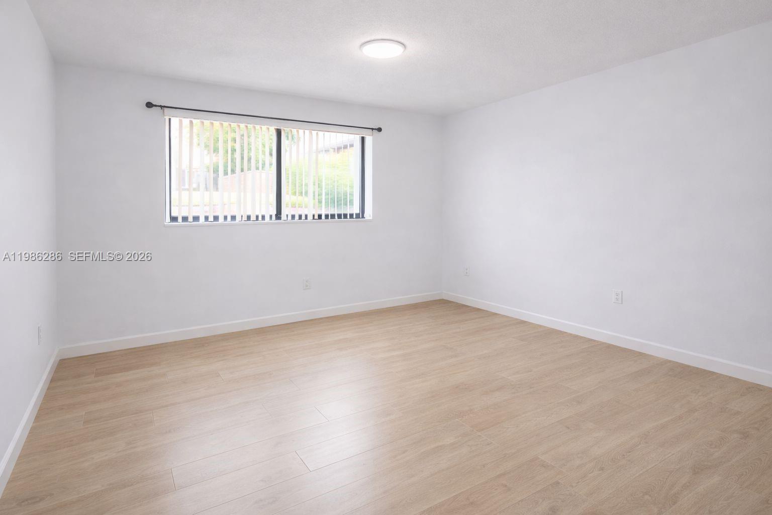 An empty bedroom features light wood-look flooring, white walls, and a window with vertical blinds — 15620 SW 80th St # 304, Kendall FL 33193, KENDALL, FL
