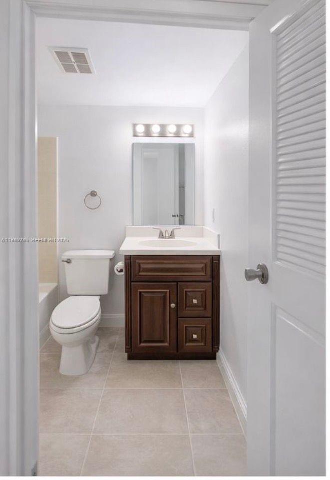 A bathroom features a white toilet, a dark wood vanity with a white countertop, and tile flooring — 15620 SW 80th St # 304, Kendall FL 33193, KENDALL, FL