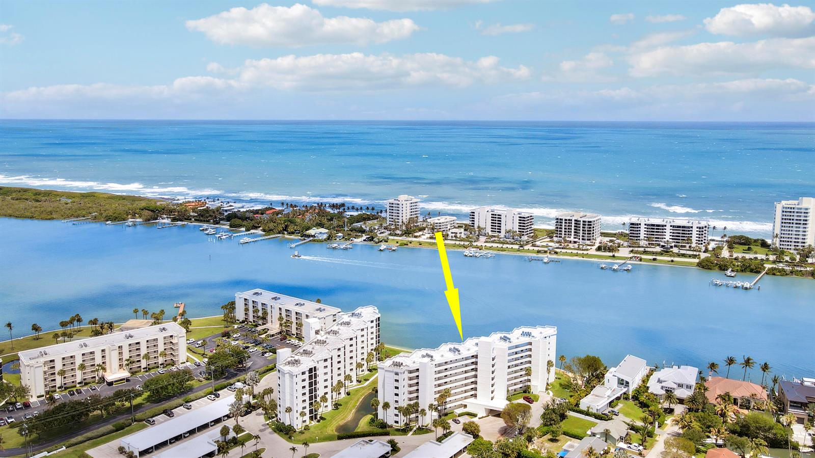 An aerial view shows a multi-story white apartment building along a waterfront with ocean views — 19800 Sandpointe Bay Drive # 708, Tequesta FL 33469, TEQUESTA, FL