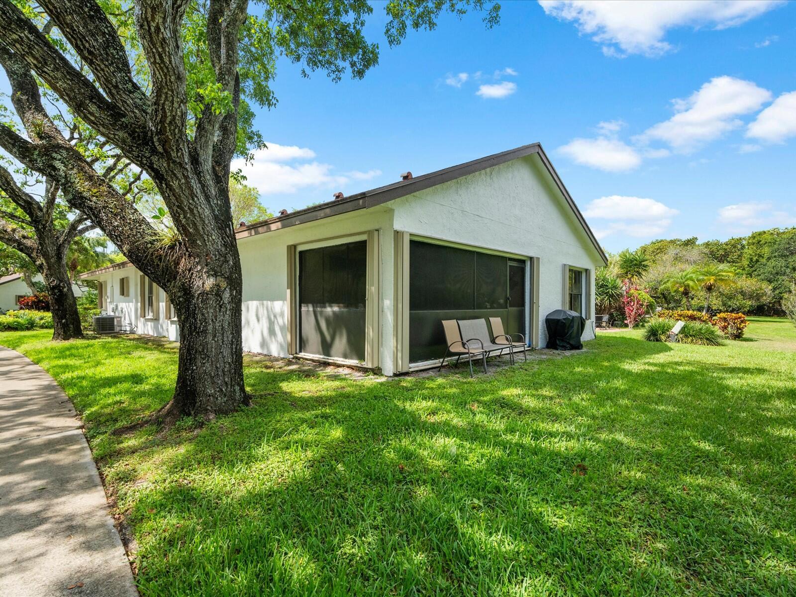 A white house with a screened-in porch sits on a grassy lawn near large trees — 2495 Dawn Tree Terrace, Coconut Creek FL 33063, COCONUT CREEK, FL