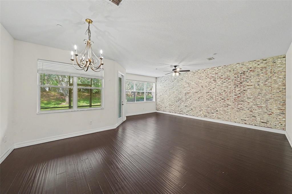 A spacious room features dark wood flooring, a textured brick accent wall, and a chandelier — 7422 TERRACE RIVER DRIVE, TEMPLE TERRACE, FL