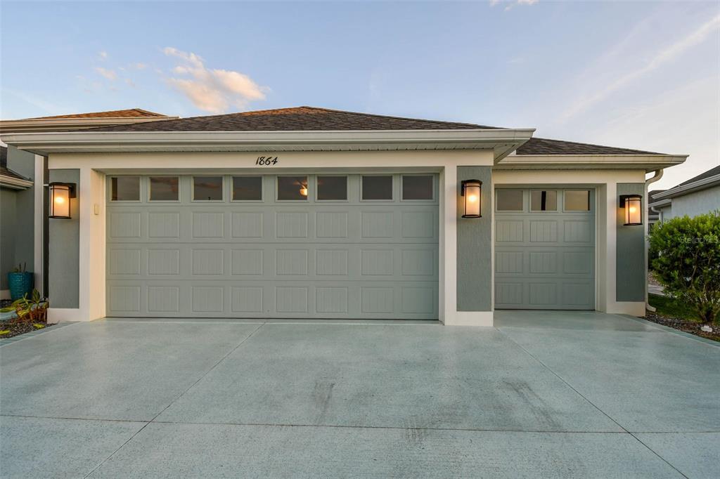 A house exterior features a two-car garage and a single-car garage with light gray doors — 1864 KEEL COURT UNIT 1, THE VILLAGES, FL