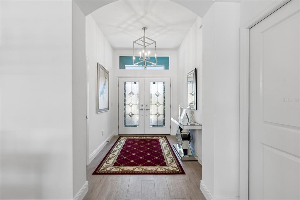 A bright entryway features a red patterned rug, a mirrored console table, and double doors — 1864 KEEL COURT UNIT 1, THE VILLAGES, FL