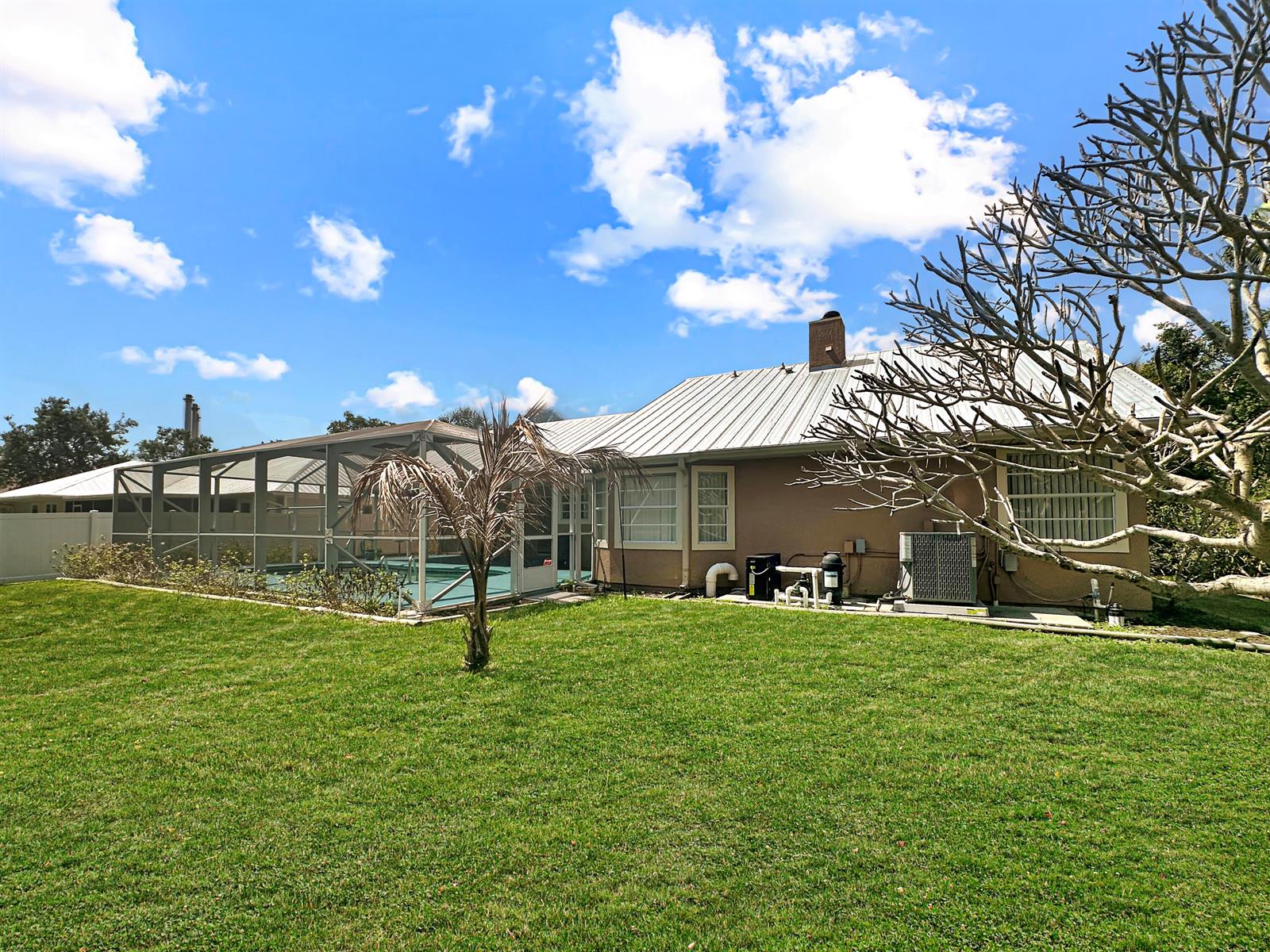 A backyard features a house with a metal roof, a screened pool enclosure, and lawn — 1860 Cobia Drive, Vero Beach FL 32960, VERO BEACH, FL