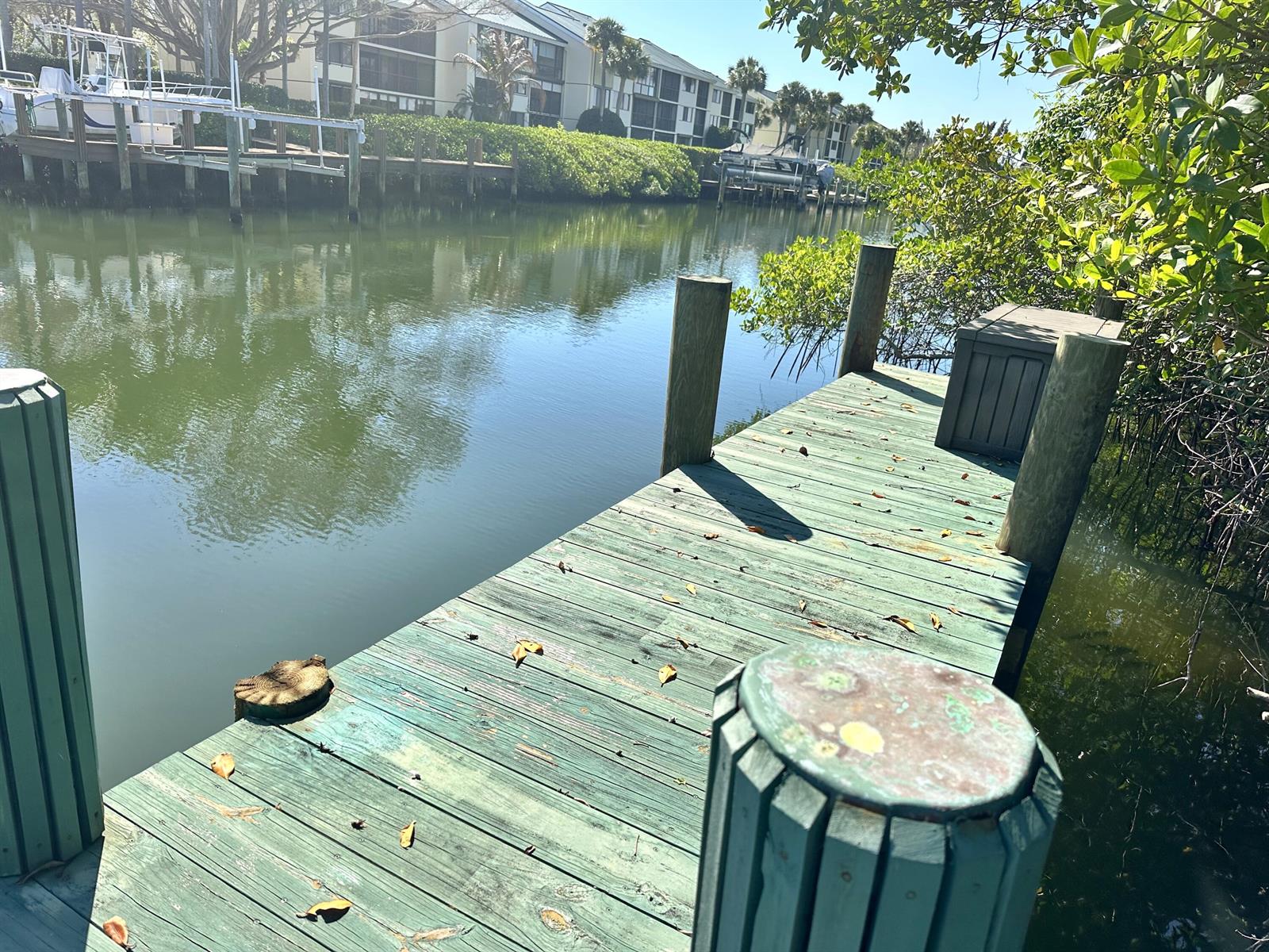 A wooden dock extends over a calm canal toward a residential building and boat slips — 1860 Cobia Drive, Vero Beach FL 32960, VERO BEACH, FL