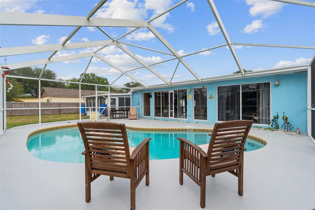 A screened-in patio features a swimming pool, two wooden chairs, and a light blue wall — 4333 71ST AVENUE N, PINELLAS PARK, FL