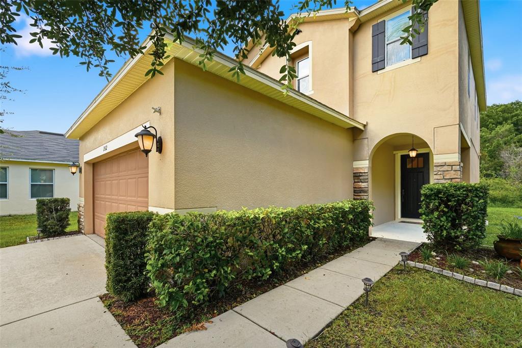 A two-story tan stucco house features a garage, a front entryway, and a landscaped hedge — 1532 NATURE TRAIL, KISSIMMEE, FL