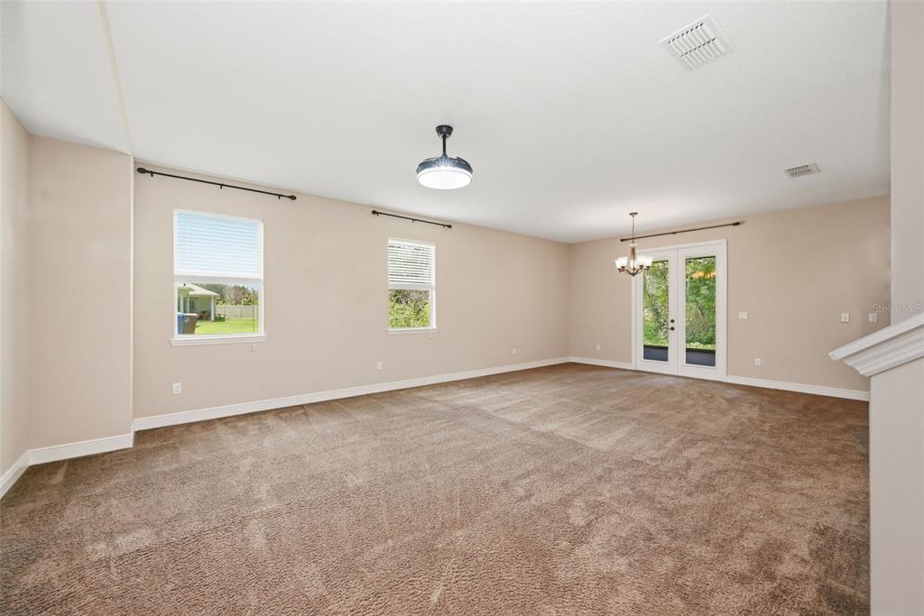 A spacious living room features beige walls, brown carpeting, two windows, and a glass door — 1532 NATURE TRAIL, KISSIMMEE, FL