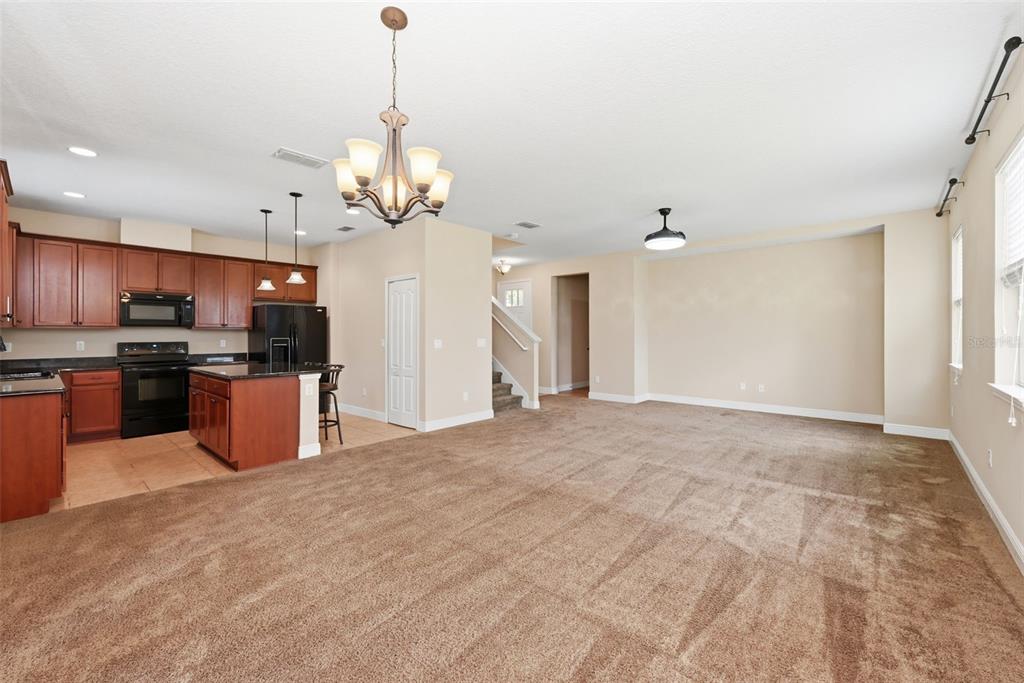 An open-concept living area features brown carpeting, a kitchen with wood cabinets, and pendant lighting — 1532 NATURE TRAIL, KISSIMMEE, FL