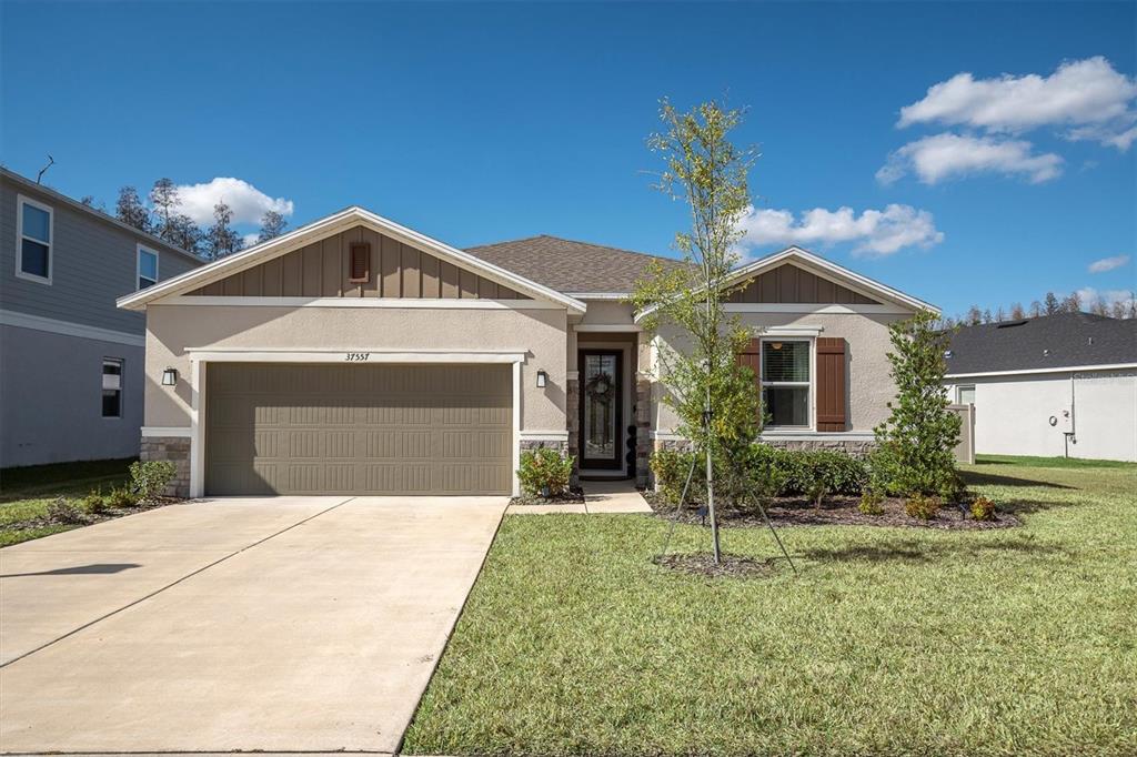A single-story house with a beige stucco exterior, a two-car garage, and a front lawn — 37557 MACKENZIE DRIVE, ZEPHYRHILLS, FL