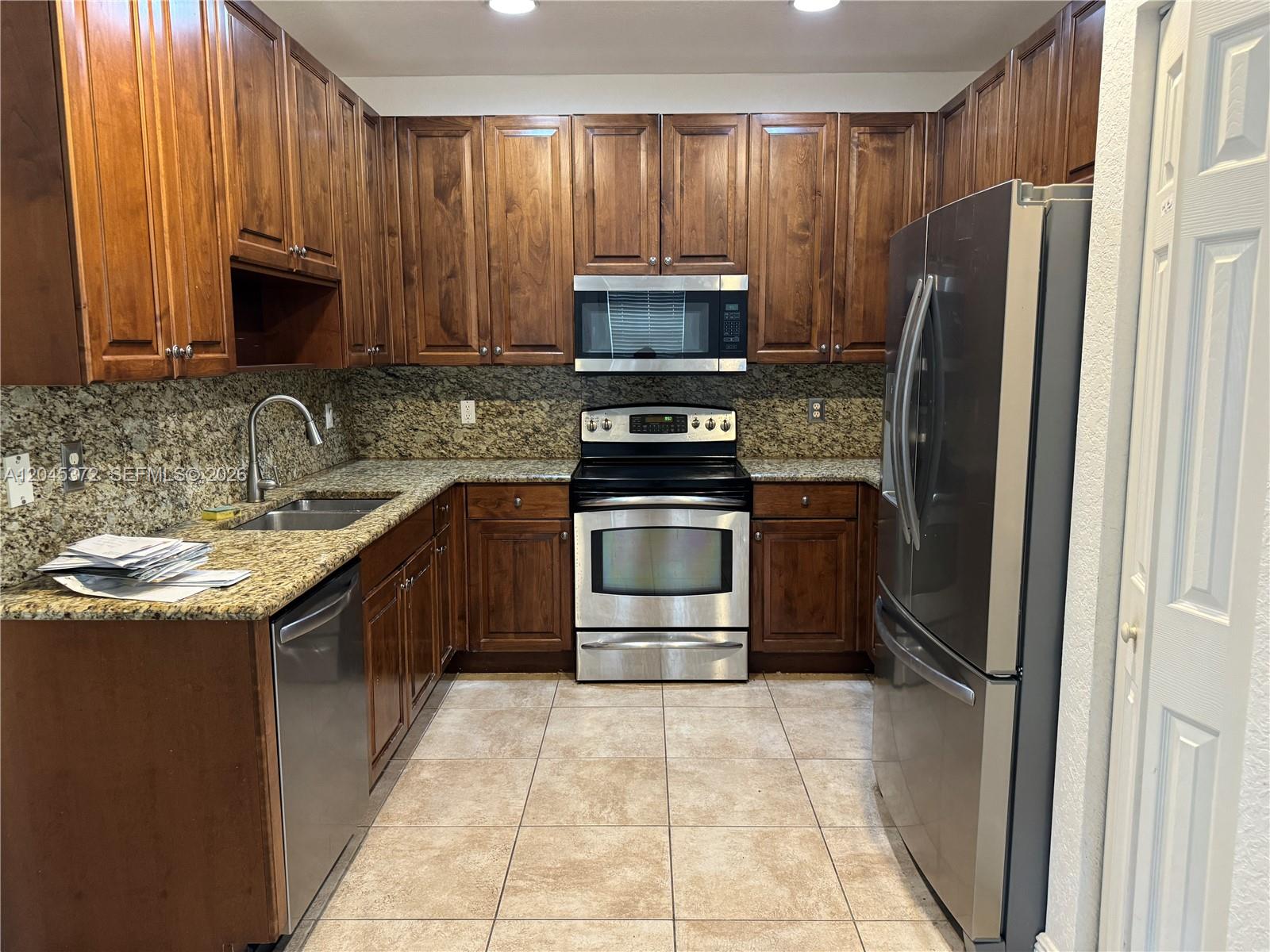A galley kitchen features dark wood cabinets, granite countertops, and stainless steel appliances — 9763 Darlington Pl # 9763, Cooper City FL 33328, COOPER CITY, FL