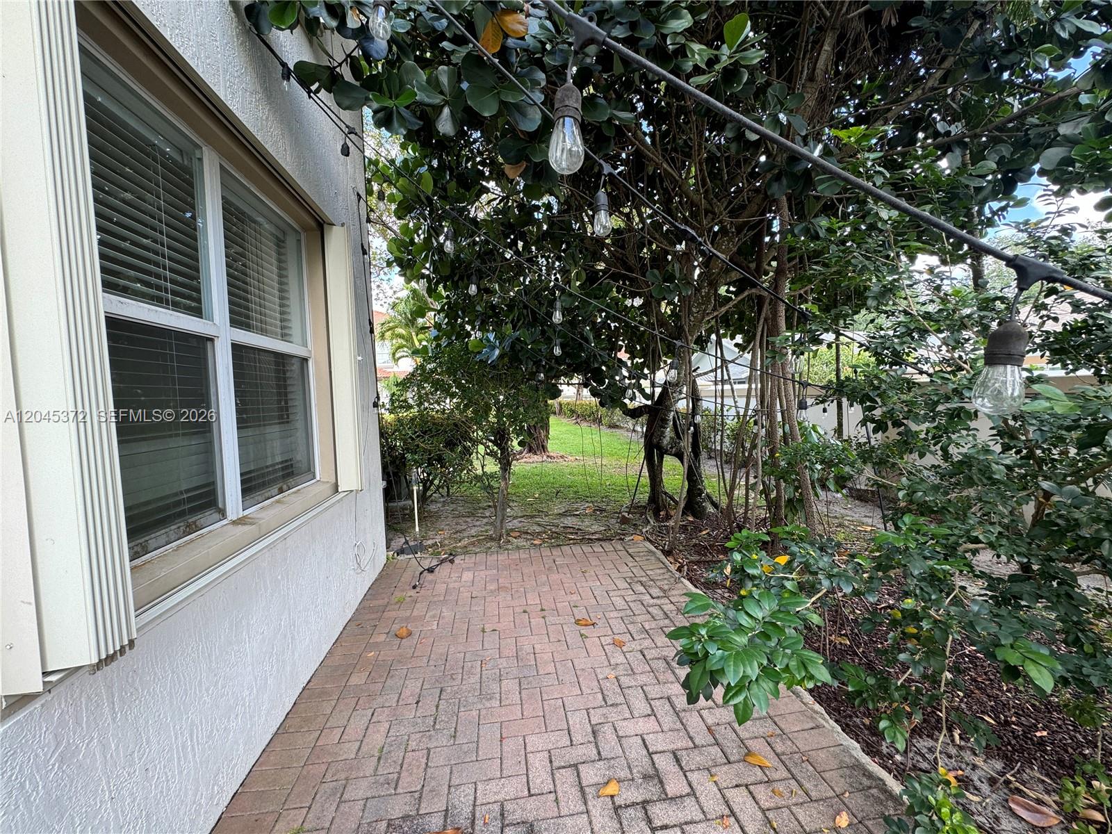 A brick patio sits beside a house wall with a window under string lights — 9763 Darlington Pl # 9763, Cooper City FL 33328, COOPER CITY, FL