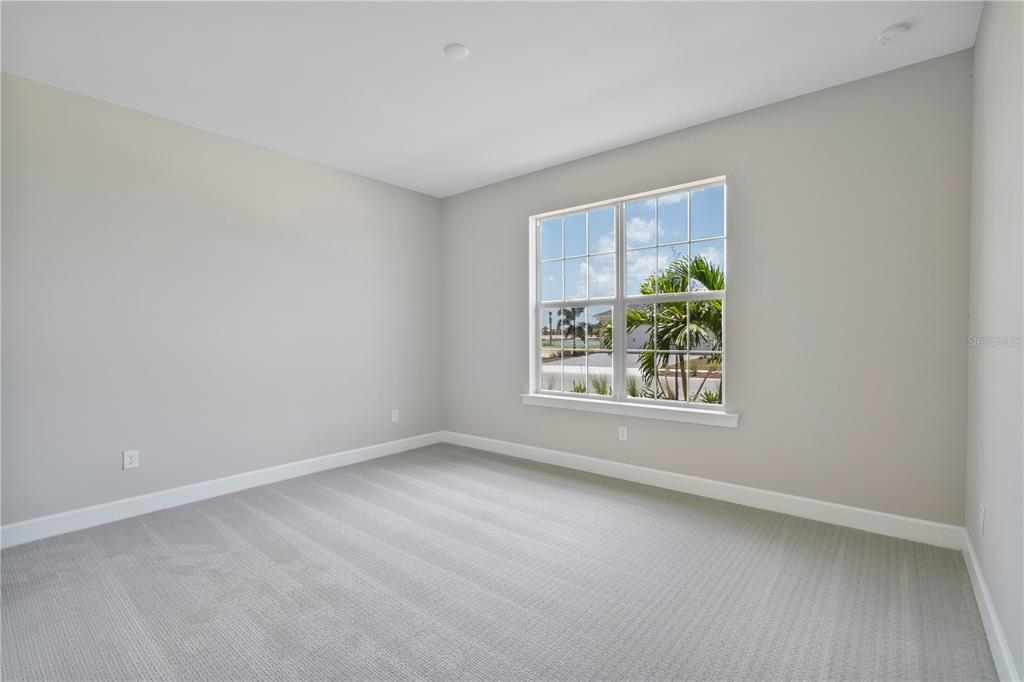 An empty bedroom with light gray walls, gray carpet, and a window overlooking palm trees — 16056 SHORELINE DRIVE, PUNTA GORDA, FL