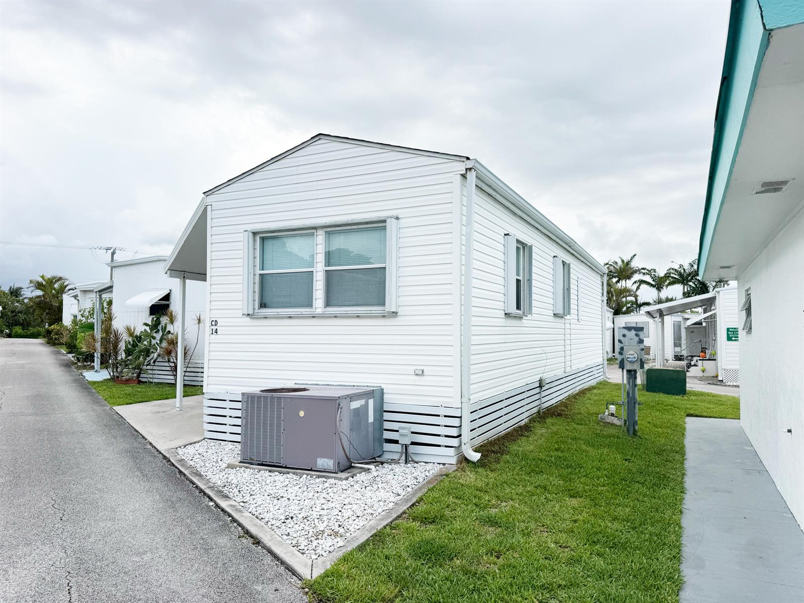 A white mobile home with a central air conditioning unit sits on a gravel pad — 14 Bamboo Drive, Briny Breezes FL 33435, BRINY BREEZES, FL