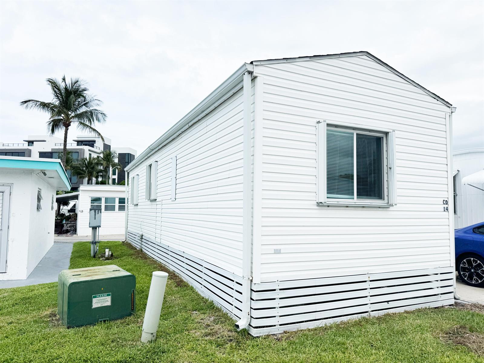 A white mobile home with horizontal siding stands on a grassy lot with utility boxes — 14 Bamboo Drive, Briny Breezes FL 33435, BRINY BREEZES, FL