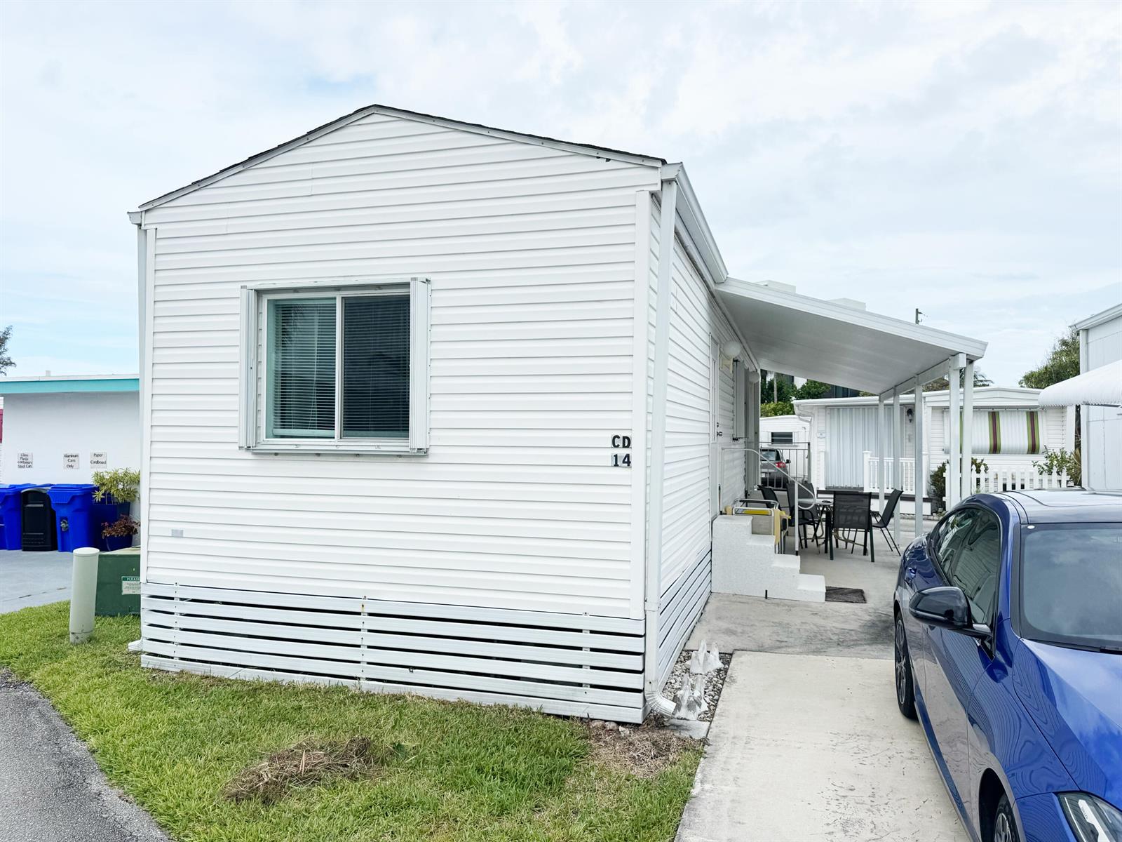 A white mobile home with a carport and a blue car parked in the driveway — 14 Bamboo Drive, Briny Breezes FL 33435, BRINY BREEZES, FL