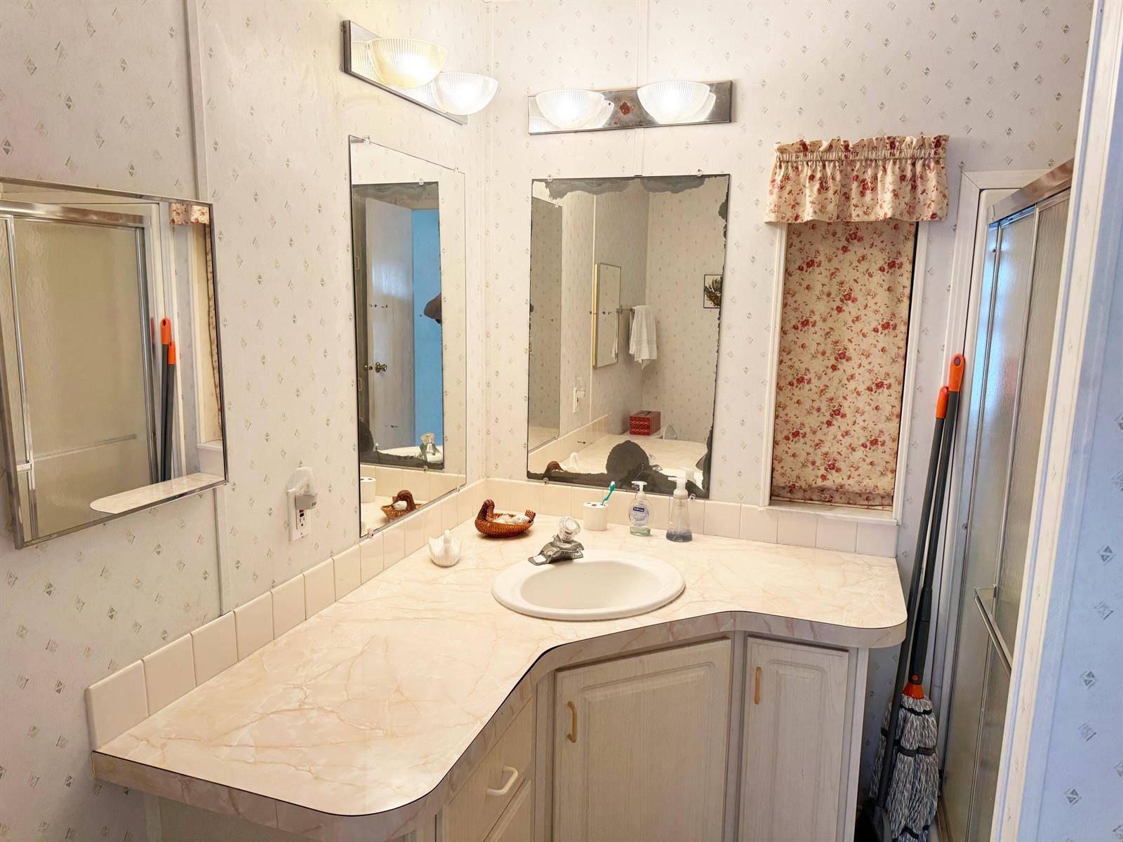 A bathroom features a corner vanity with a marble-look countertop, floral wallpaper, and two mirrors — 14 Bamboo Drive, Briny Breezes FL 33435, BRINY BREEZES, FL