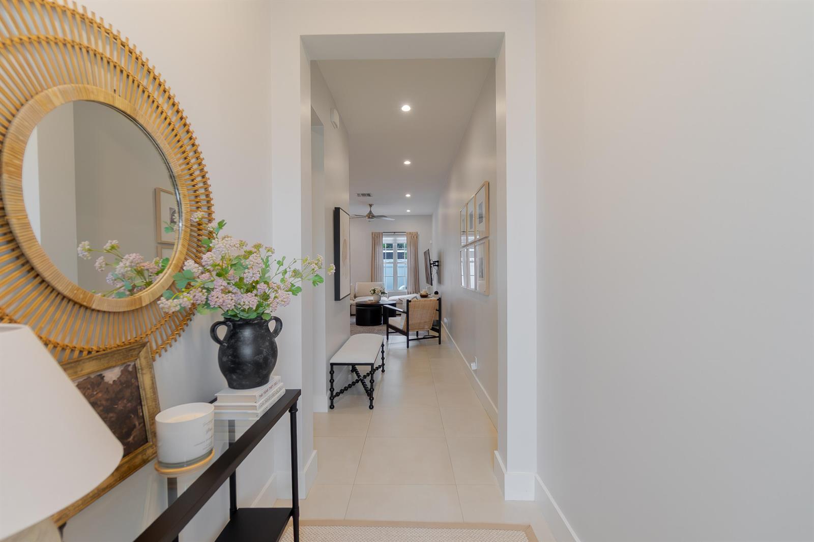 A hallway with light tile flooring leads from a decorated entryway into a living room — 918 St George Boulevard, Delray Beach FL 33483, DELRAY BEACH, FL