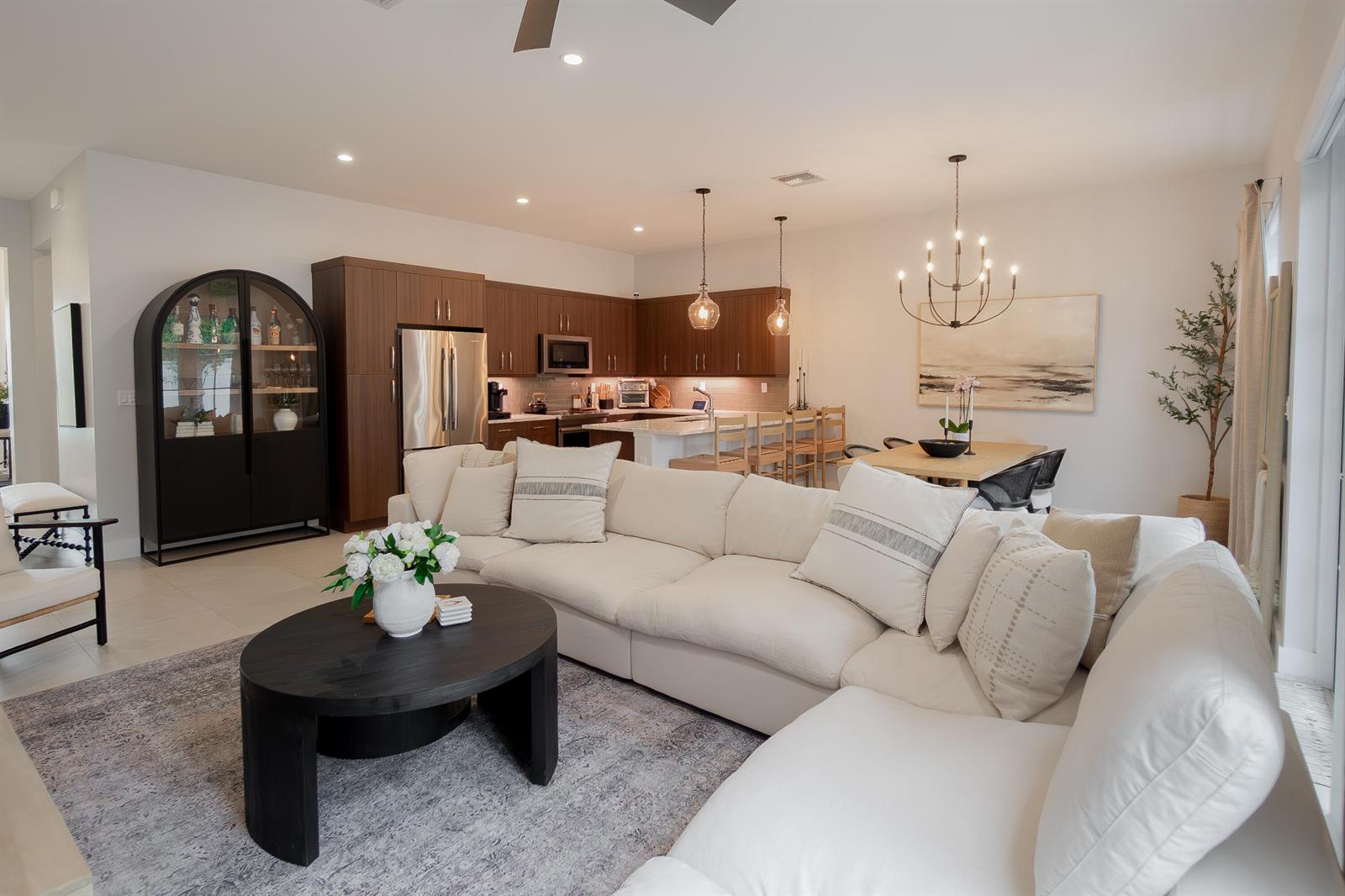 An open-concept living room and kitchen featuring a white sectional, dark cabinets, and dining area — 918 St George Boulevard, Delray Beach FL 33483, DELRAY BEACH, FL