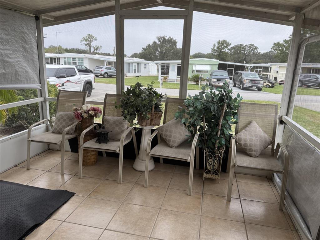 A screened-in porch features four patio chairs with pillows and potted plants on tiled flooring — 9072 LAKE POINT BOULEVARD, LAKE WALES, FL