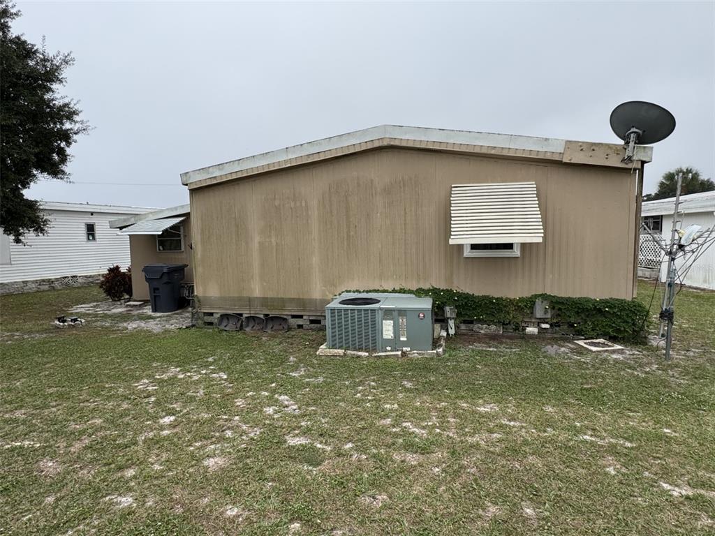 The exterior of a tan mobile home features an air conditioning unit and a window awning — 9072 LAKE POINT BOULEVARD, LAKE WALES, FL