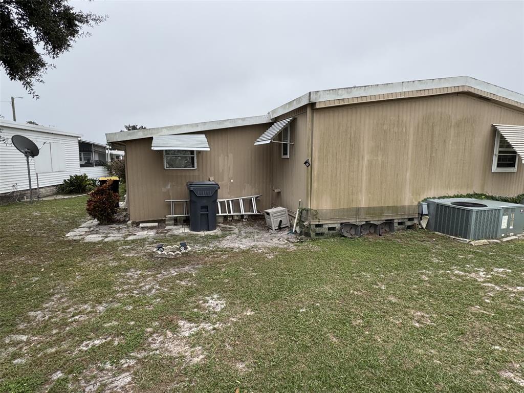 The exterior of a tan mobile home features a metal awning, air conditioning unit, and yard — 9072 LAKE POINT BOULEVARD, LAKE WALES, FL