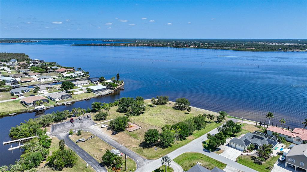 An aerial view shows a waterfront lot with a playground, parking area, and nearby houses — 12121 SNOW BIRD AVENUE, PORT CHARLOTTE, FL