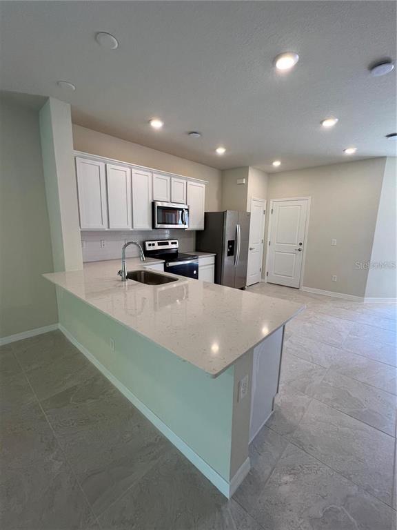 A kitchen features white cabinets, stainless steel appliances, and a quartz-topped island with a sink — 4793 SPARKLING SHELL AVENUE, KISSIMMEE, FL