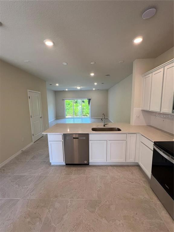 A kitchen with white cabinets, stainless steel appliances, and light tile flooring overlooks a living area — 4793 SPARKLING SHELL AVENUE, KISSIMMEE, FL