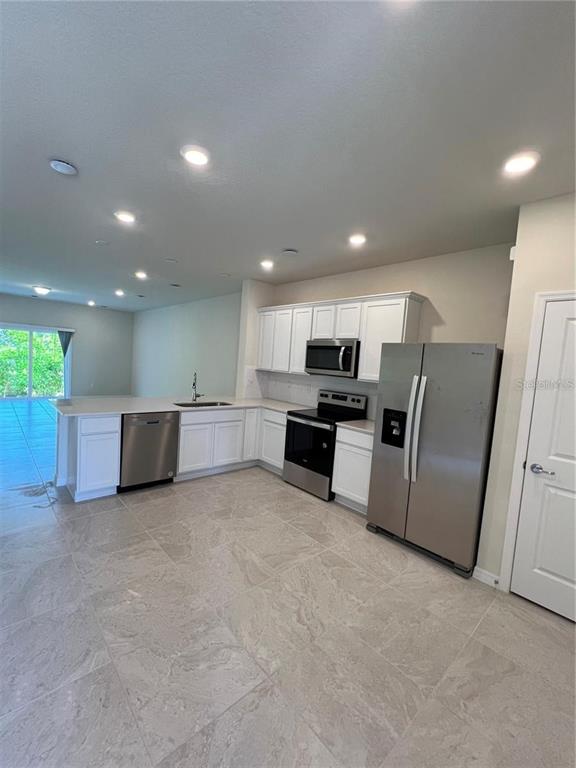 A kitchen features white cabinets, stainless steel appliances, and light-colored tile flooring — 4793 SPARKLING SHELL AVENUE, KISSIMMEE, FL