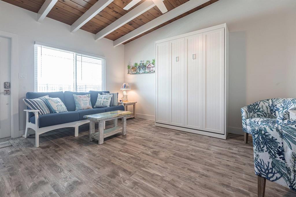 A living room features a blue sofa, a white Murphy bed, and wood-look flooring — 6006 MIDNIGHT PASS ROAD UNIT 29, SARASOTA, FL