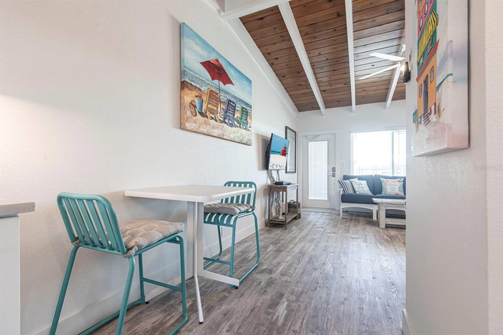 A small dining area with teal chairs leads into a living room with wood ceilings — 6006 MIDNIGHT PASS ROAD UNIT 29, SARASOTA, FL