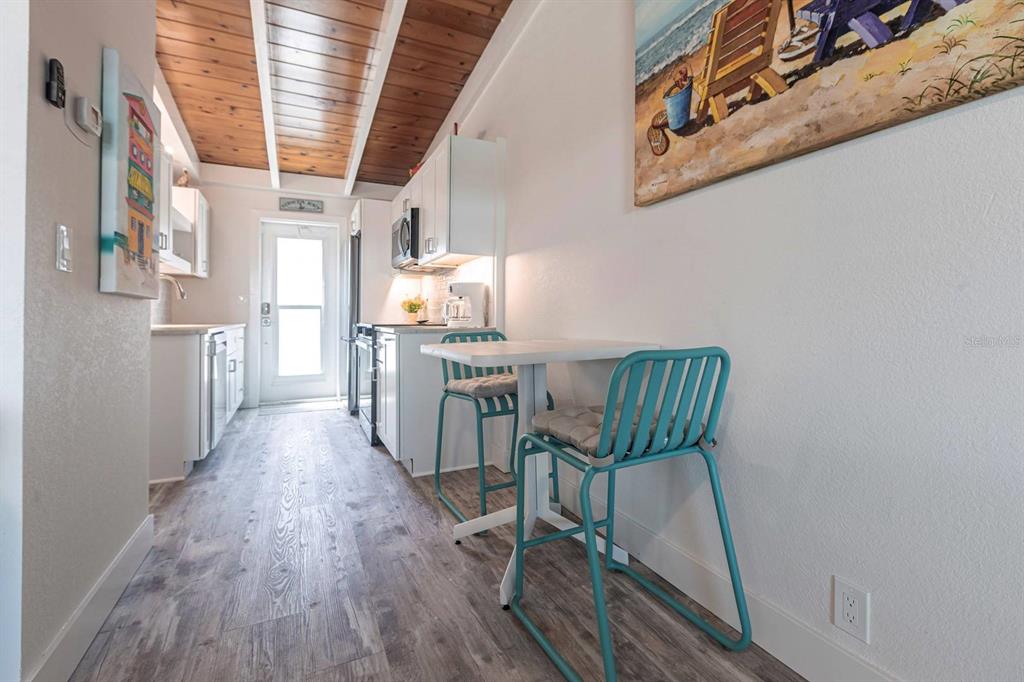 A narrow kitchen features white cabinetry, wood-paneled ceilings, and a small dining table with stools — 6006 MIDNIGHT PASS ROAD UNIT 29, SARASOTA, FL