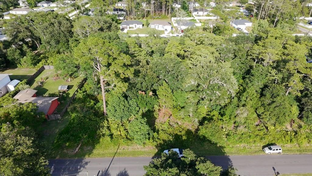 An aerial view shows a wooded, undeveloped residential lot situated between houses and a road — 2057 8TH AVENUE, DELAND, FL