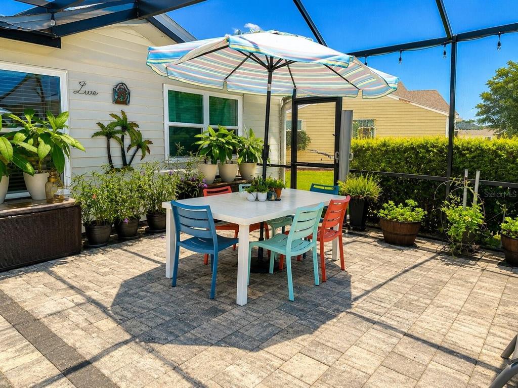 A patio with a white dining table, colorful chairs, and a striped umbrella inside a screen enclosure — 1018 PARAKEET TRAIL, LAKELAND, FL