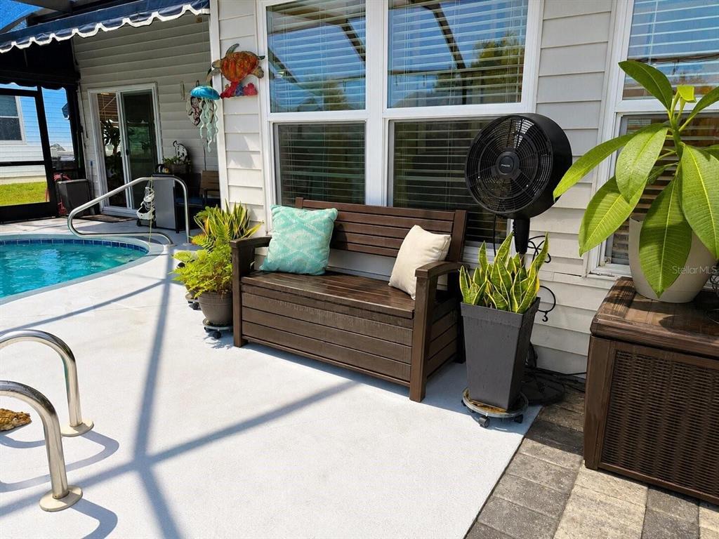 A wooden bench with two pillows sits on a patio beside a pool and fan — 1018 PARAKEET TRAIL, LAKELAND, FL