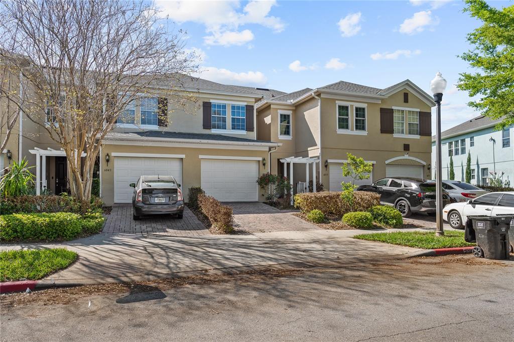 A two-story townhouse complex features beige stucco walls, white garage doors, and paved driveways — 6039 STRADA ISLE WAY, ORLANDO, FL