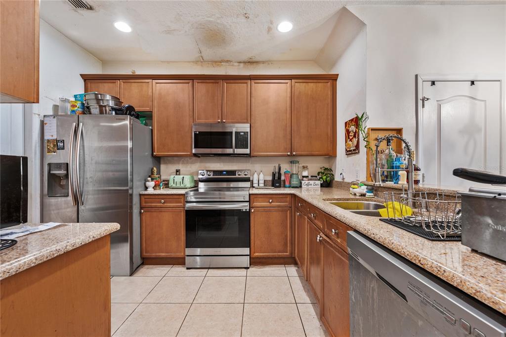 A kitchen features wood cabinets, stainless steel appliances, granite countertops, and visible ceiling water damage — 6039 STRADA ISLE WAY, ORLANDO, FL