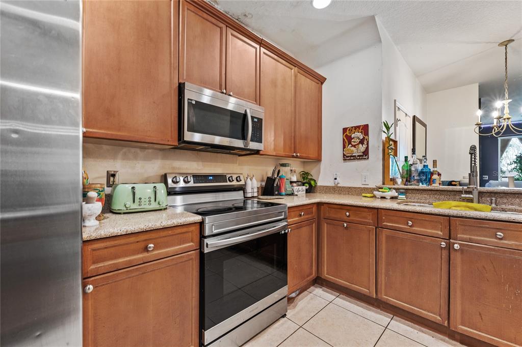 A kitchen features wood cabinets, stainless steel appliances, granite countertops, and light-colored tile flooring — 6039 STRADA ISLE WAY, ORLANDO, FL