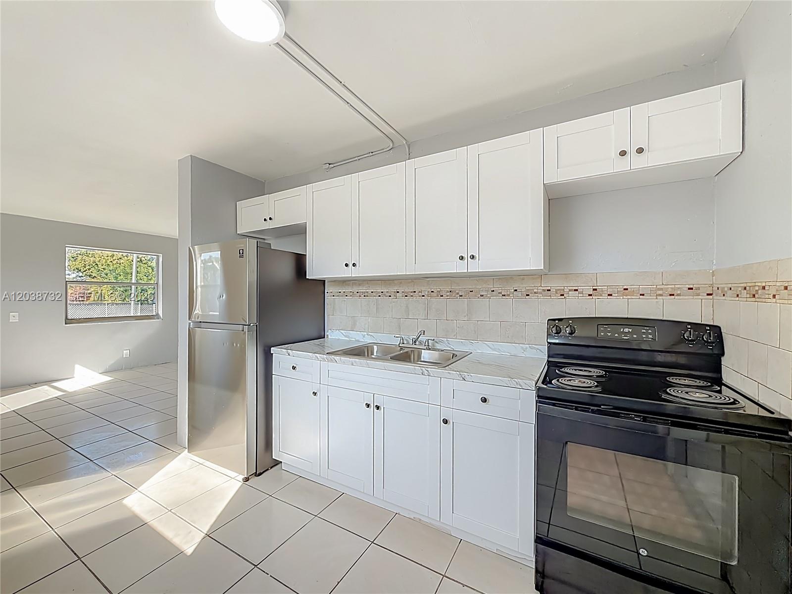 A kitchen features white cabinets, a stainless steel refrigerator, a black stove, and tiled floors — 2408 NW 8th St # 0, Pompano Beach FL 33069, POMPANO BEACH, FL