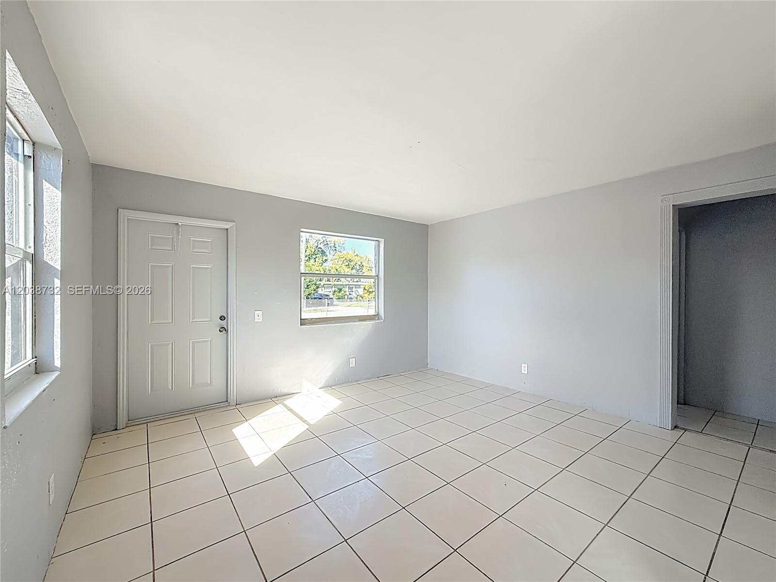 An empty room features light gray walls, white tile flooring, a door, and two windows — 2408 NW 8th St # 0, Pompano Beach FL 33069, POMPANO BEACH, FL