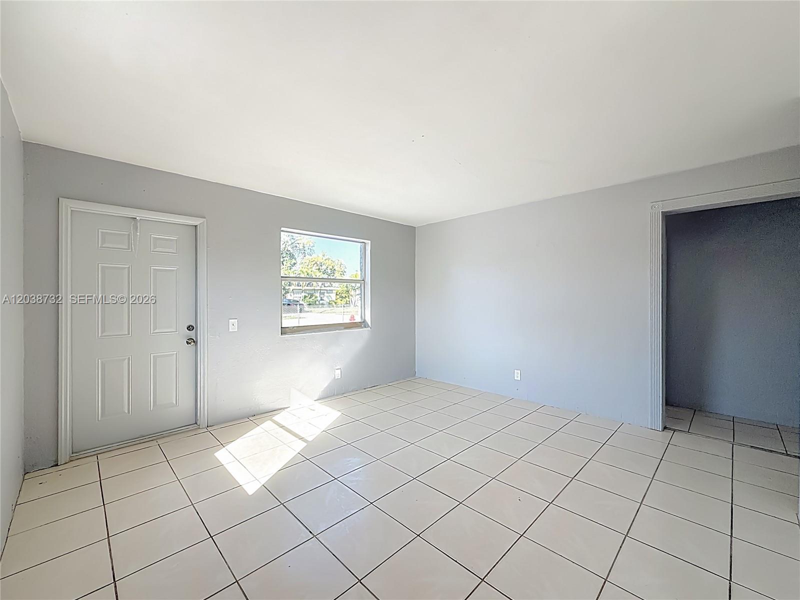 An empty room features light gray walls, white tile flooring, a window, and a doorway — 2408 NW 8th St # 0, Pompano Beach FL 33069, POMPANO BEACH, FL