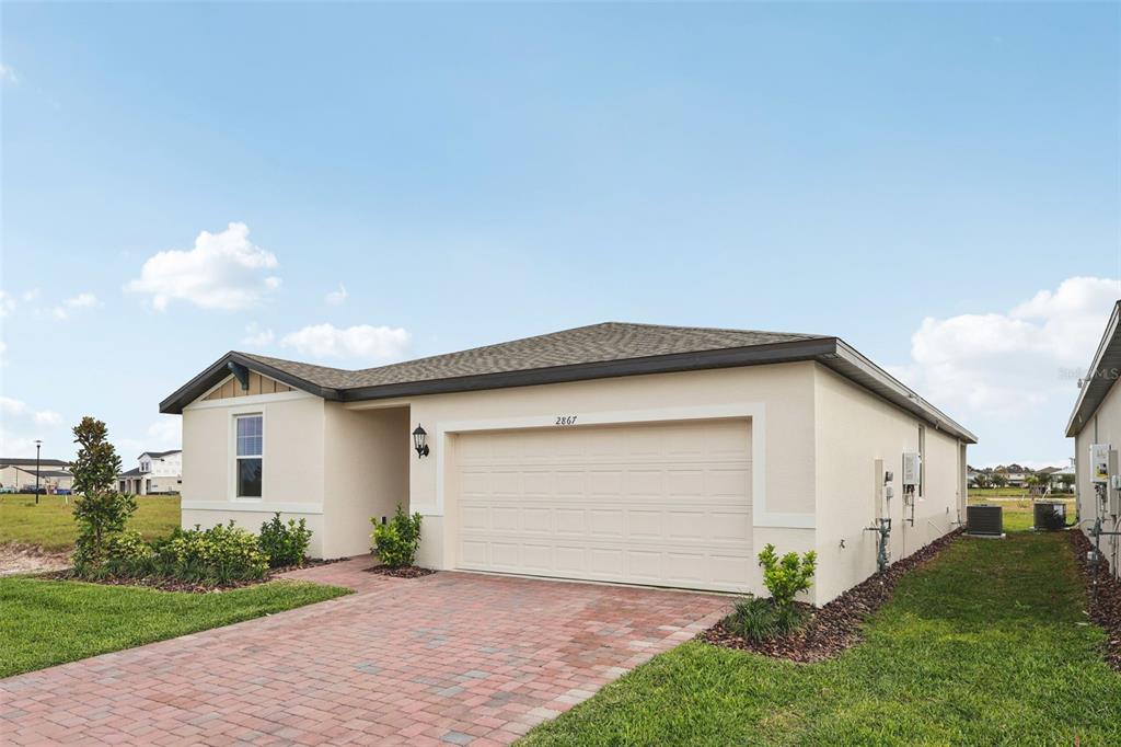 A single-story house with a beige stucco exterior, a two-car garage, and a brick driveway — 2867 HORNBILL DRIVE, ST CLOUD, FL